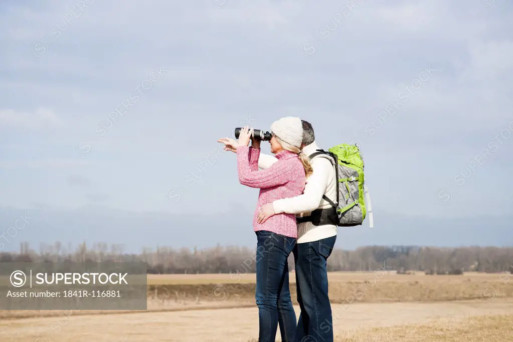 Couple standing in meadow with binoculars