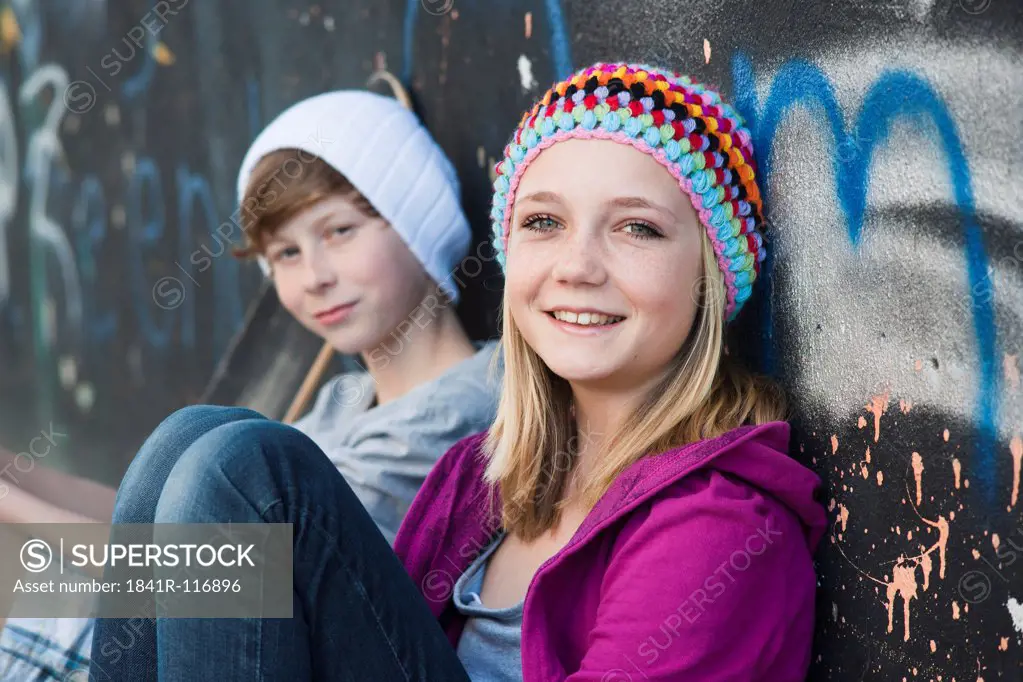 Teeange girl and boy sitting at graffiti wall