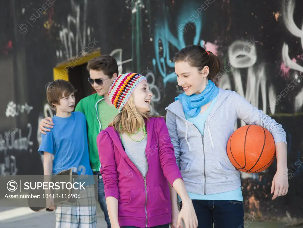 Four happy teenage friends walking at graffiti wall