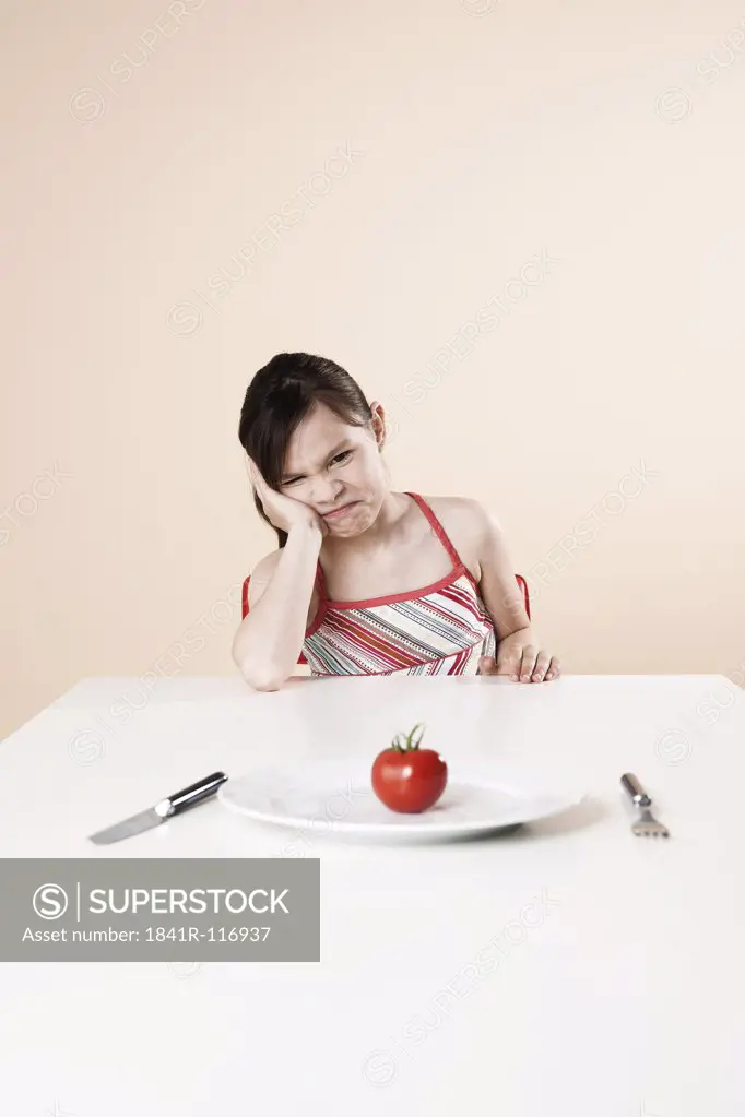 Sulking girl sitting at table with tomato