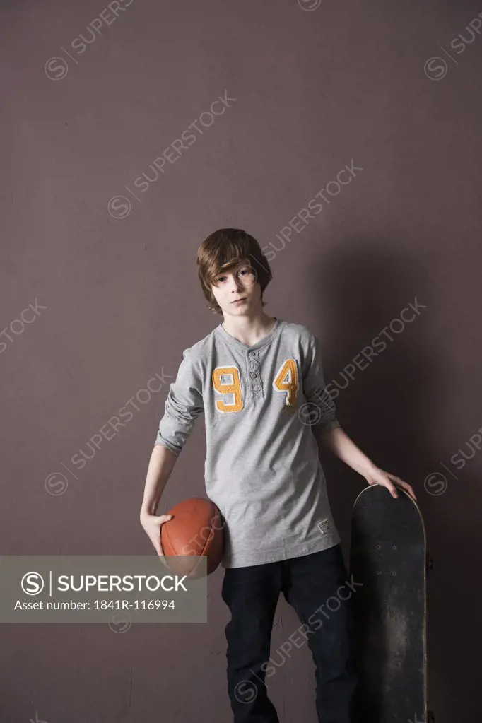 Teenage boy holding football and skateboard
