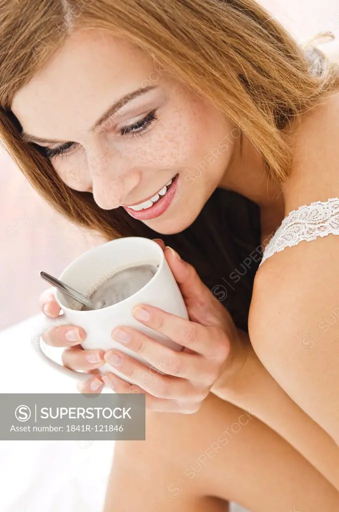 Smiling young woman with cup in bed