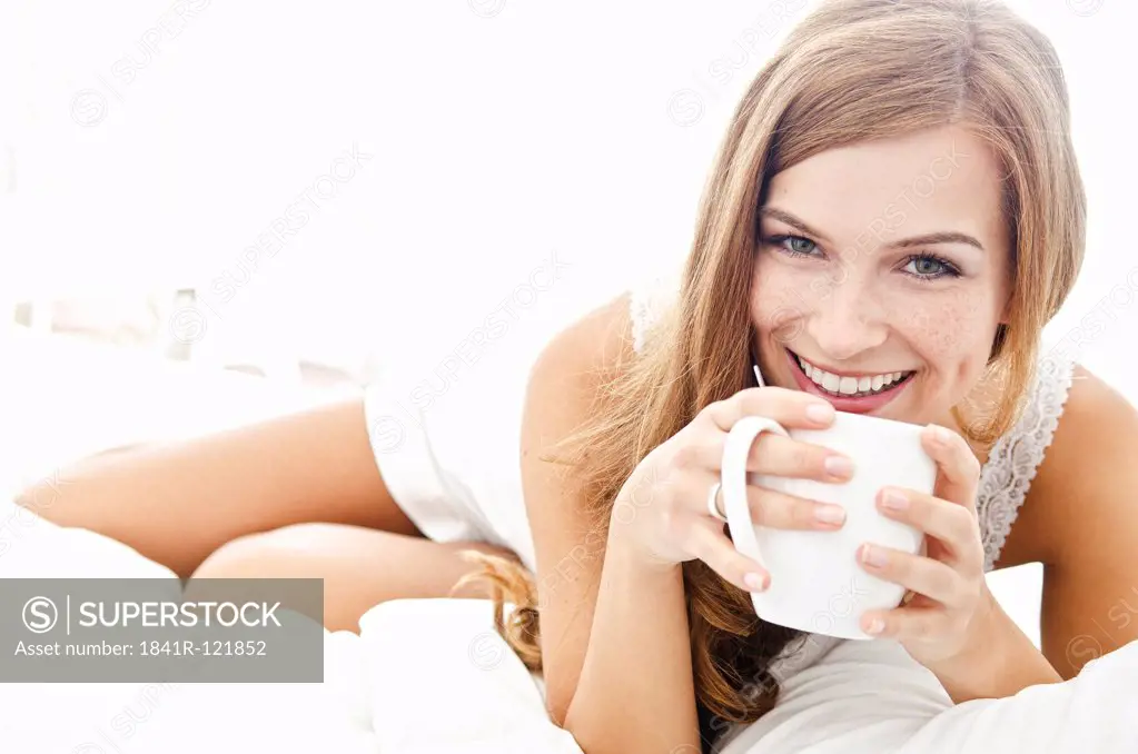 Smiling young woman with cup in bed