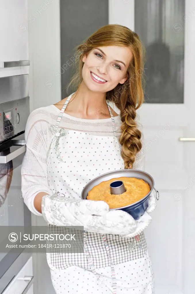 Smiling young woman with cake in kitchen