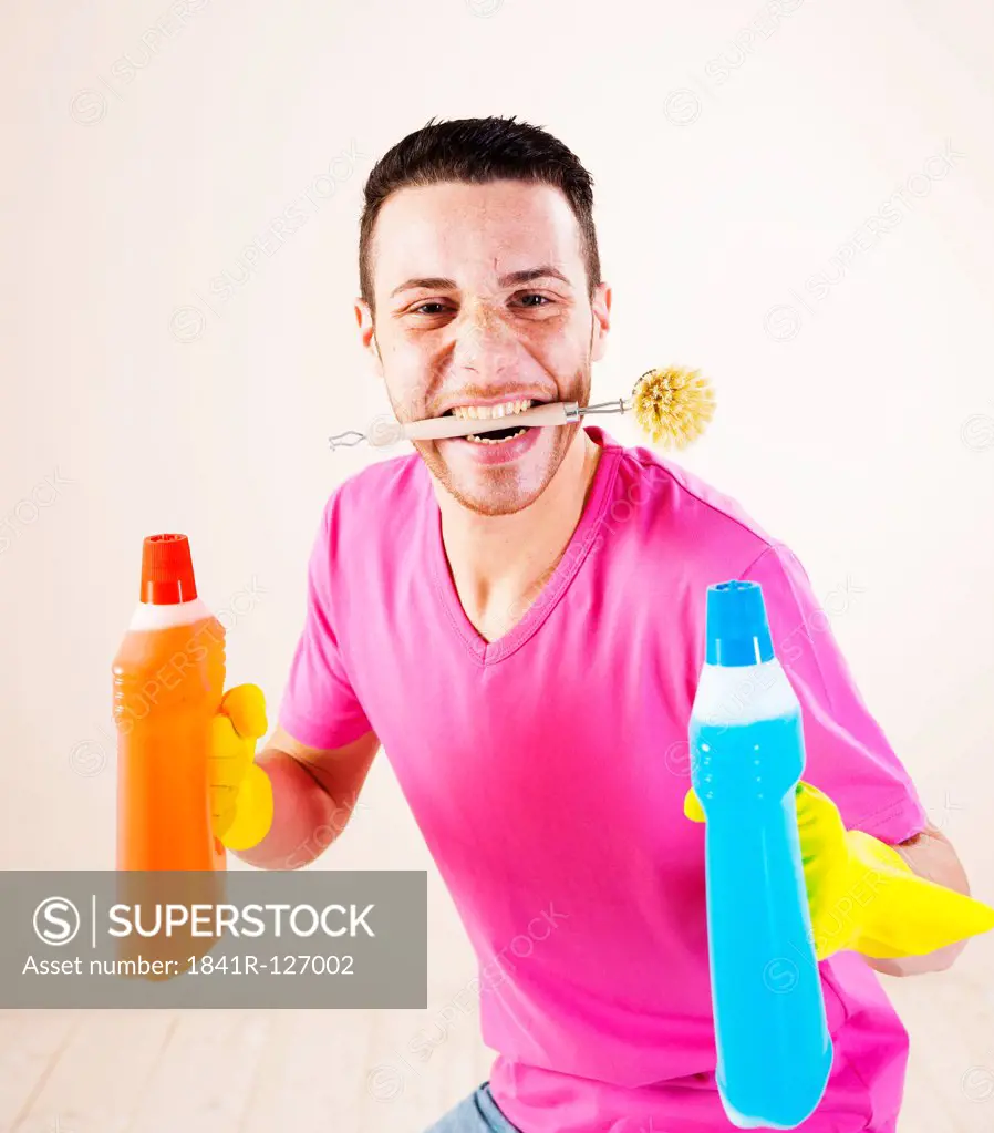 Happy young man holding cleaning agents and brush