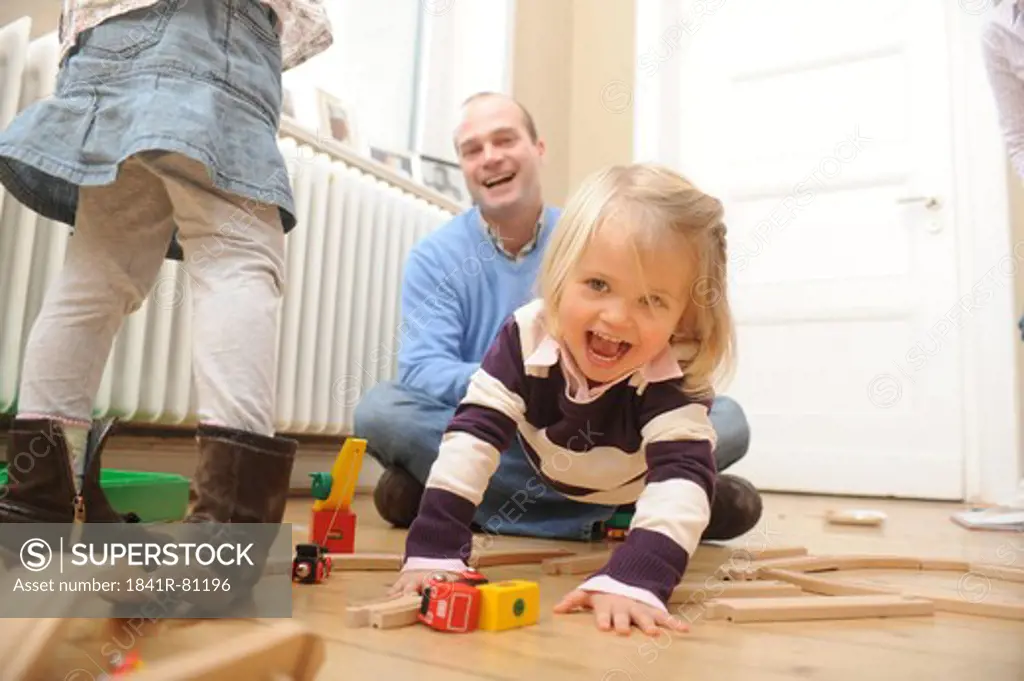 Girl playing with toys and her father playfully pulling her