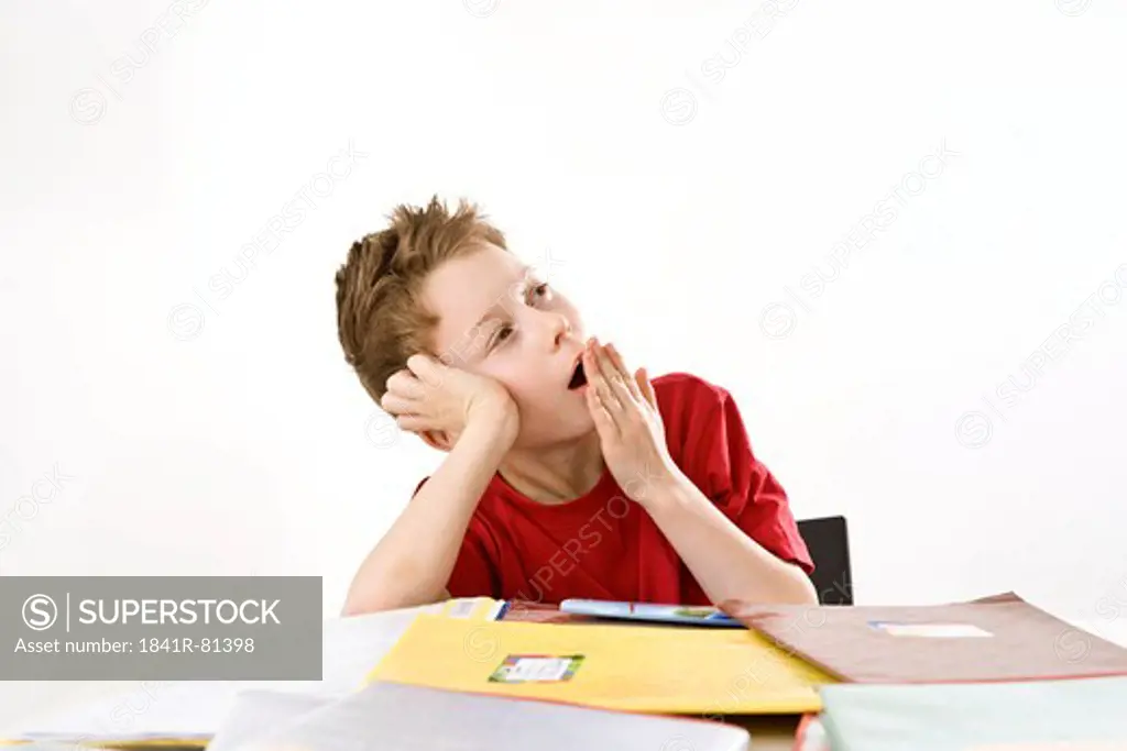 Boy leaning on books and yawning