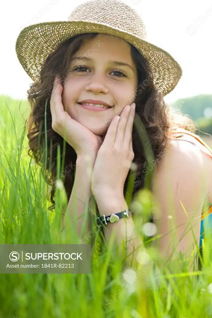 Young girl with straw hat lying in a rich green meadow, eye contact