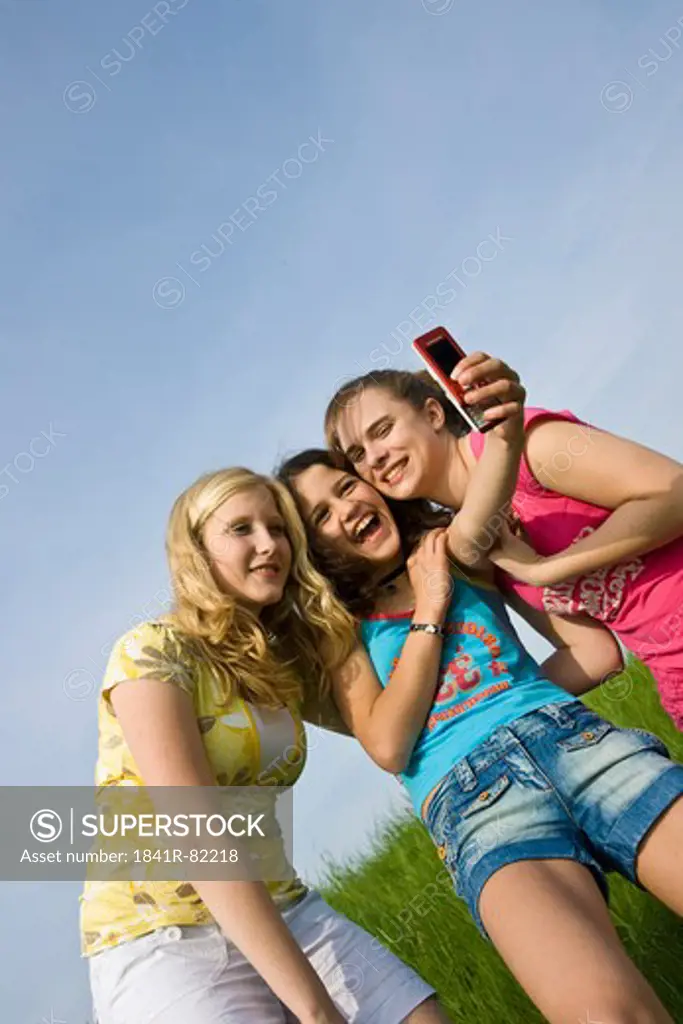 Three young girls are taking photos of themselves, low angle view