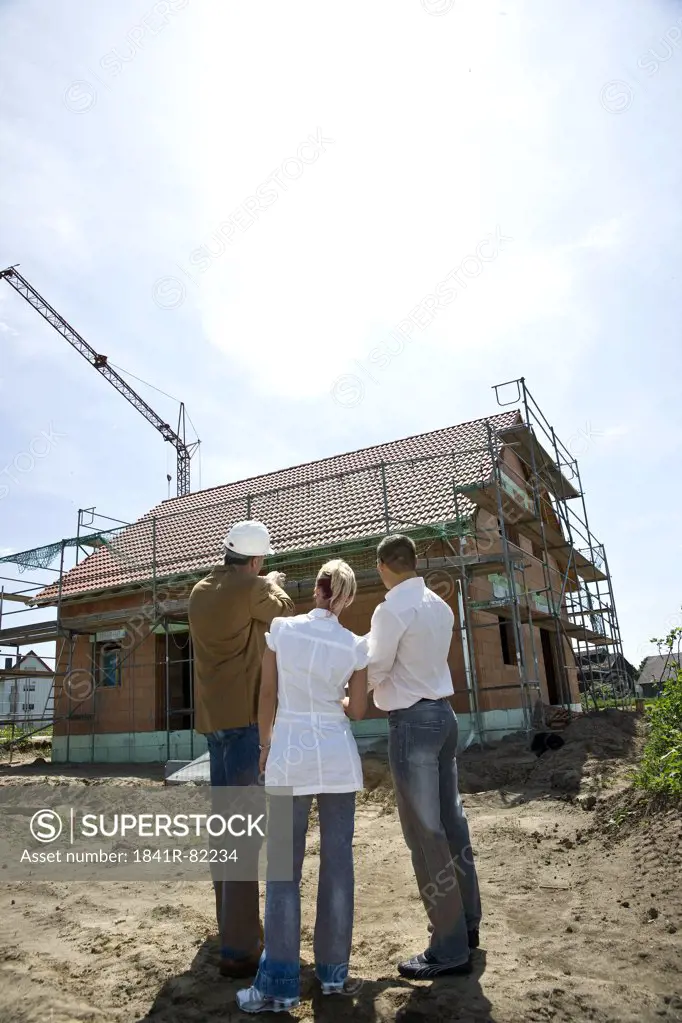 Couple talking with architect at a construction site, rear view