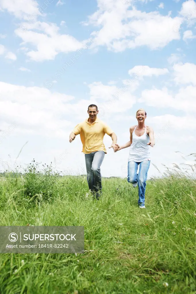 Couple running over a meadow, low angle view, front view