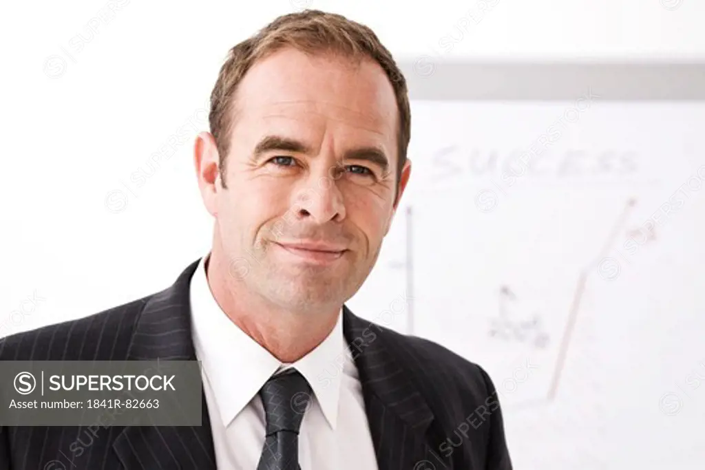 Businessman standing in front of a flip chart, facing camera, close-up