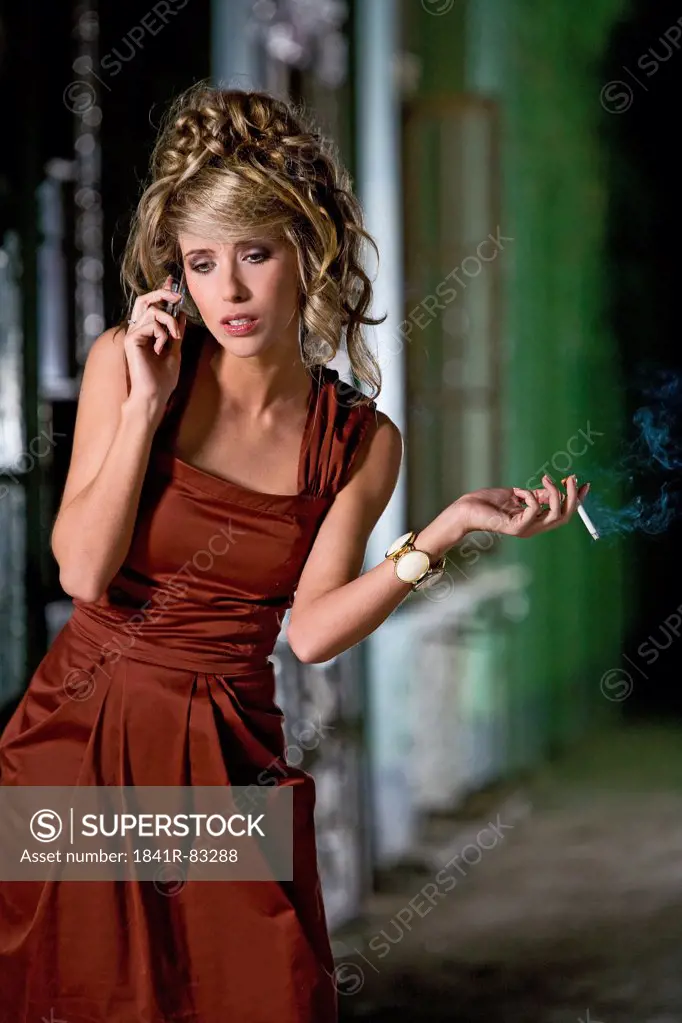 Woman in red evening dress holding a cigarette and using a cell phone