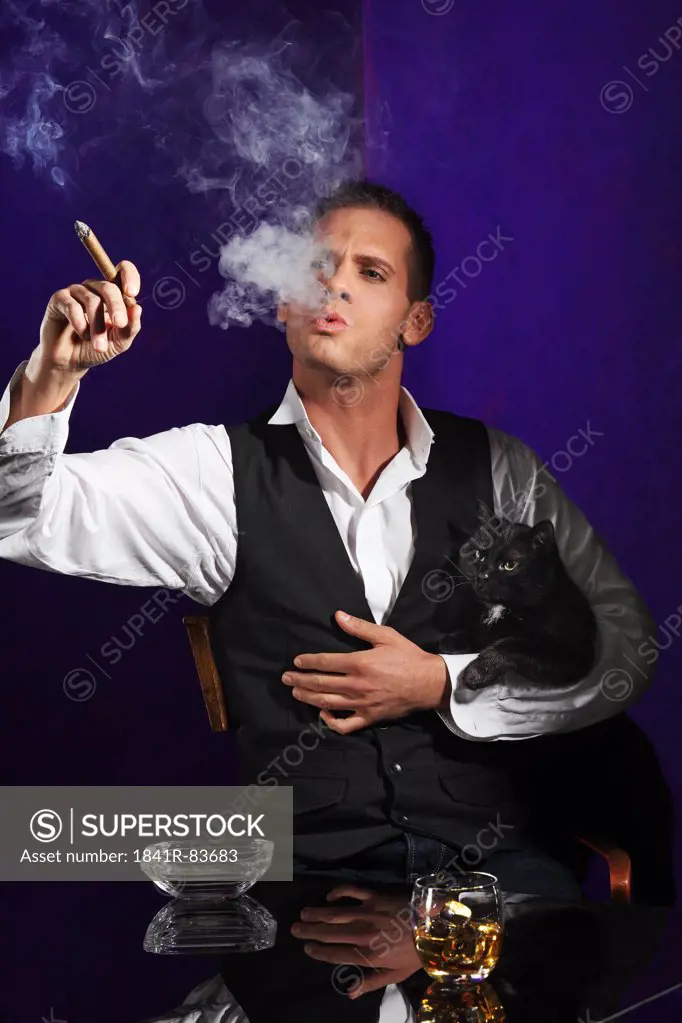 Young man with a cat in his arm smoking a cigar
