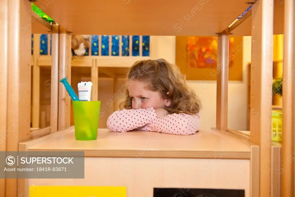 Young girl leaning against a shelf beside a toothbrush holder