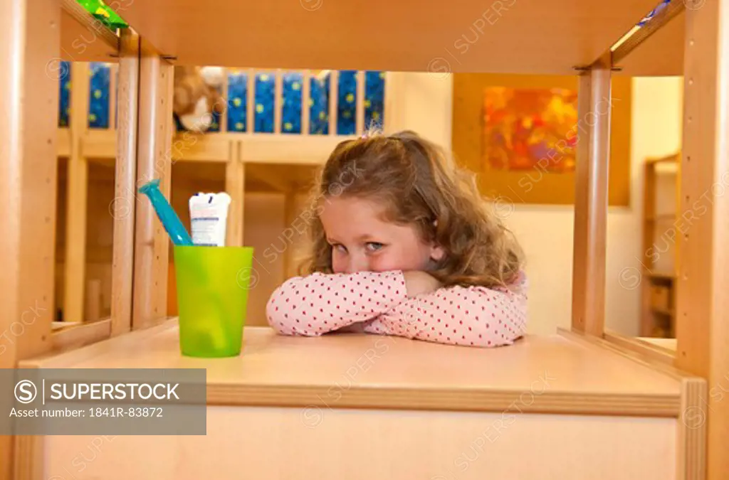 Young girl leaning against a shelf beside a toothbrush holder