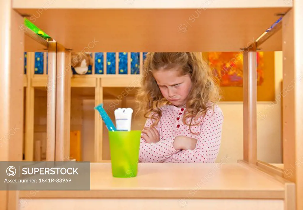 Little girl crossing arms and looking at toothbrush holder on a shelf