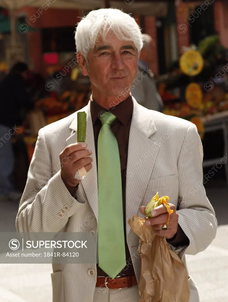 Senior man eating vegetables in town, Italy