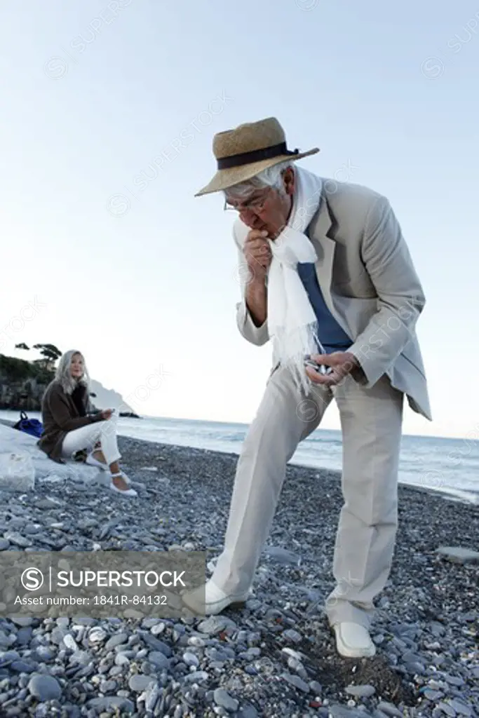 Senior man looking at stones on beach, Italy