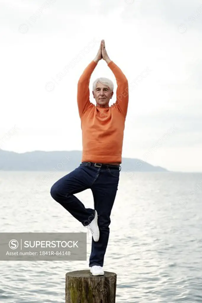 Senior man practicing yoga by the water, Italy