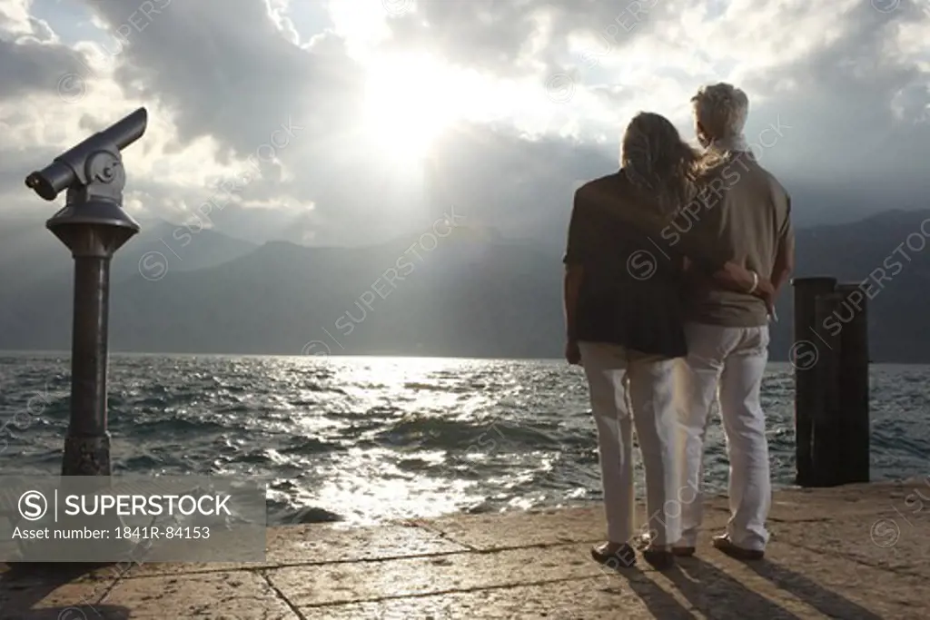 Senior couple at sunset looking on water, Italy