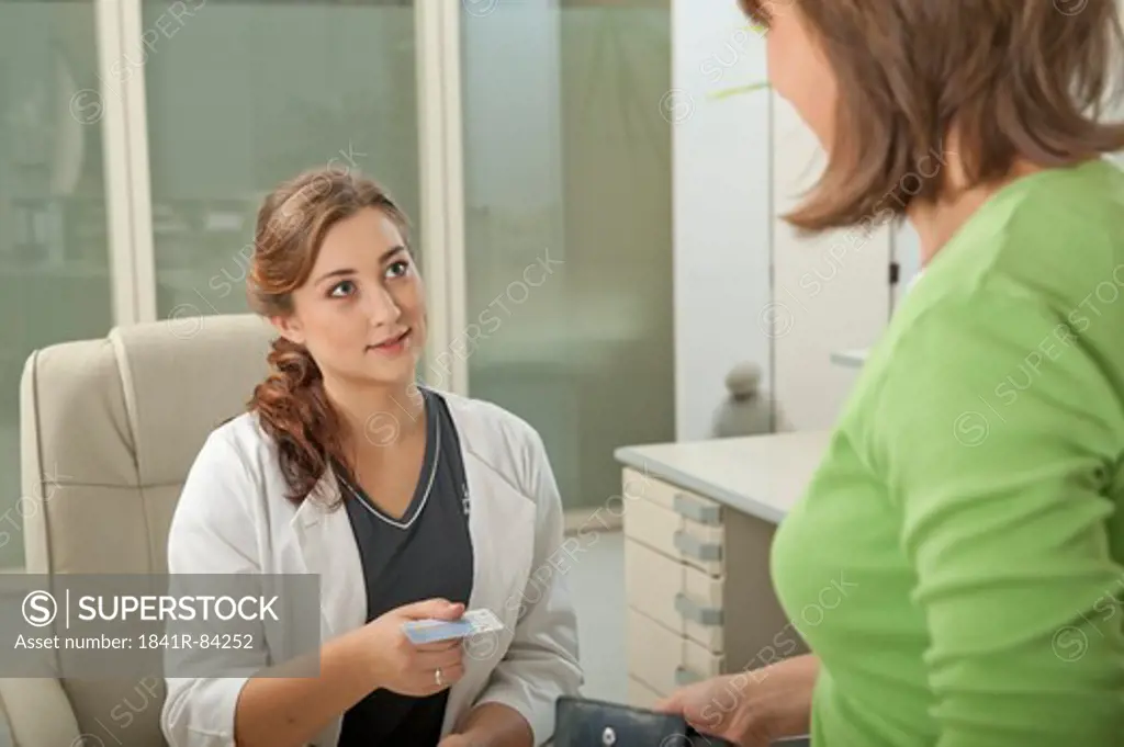 Female patient and doctor's assistant at desk with health insurance card