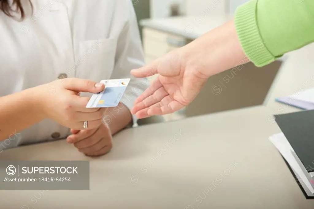 Female patient handing over health insurance card to doctor's assistant at desk