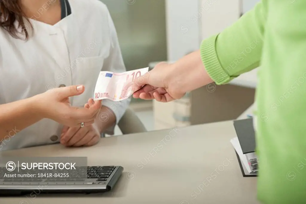 Female patient handing over ten Euro to doctor's assistant at desk
