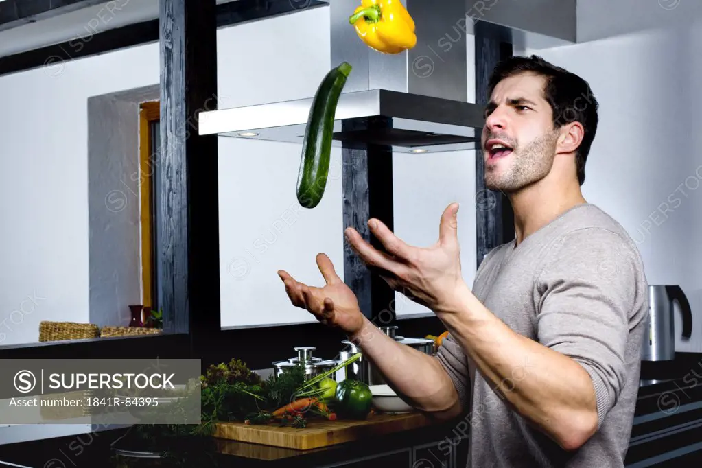 Young man juggling with cucumber and yellow pepper