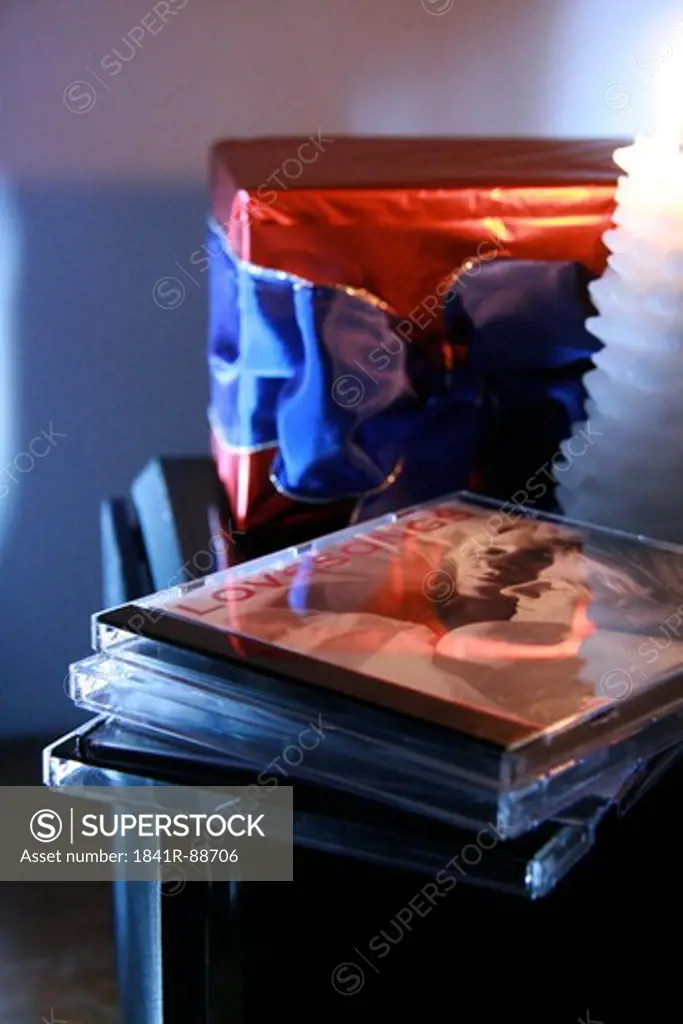 Close-up of stack of cd with lit candle and gift box on table