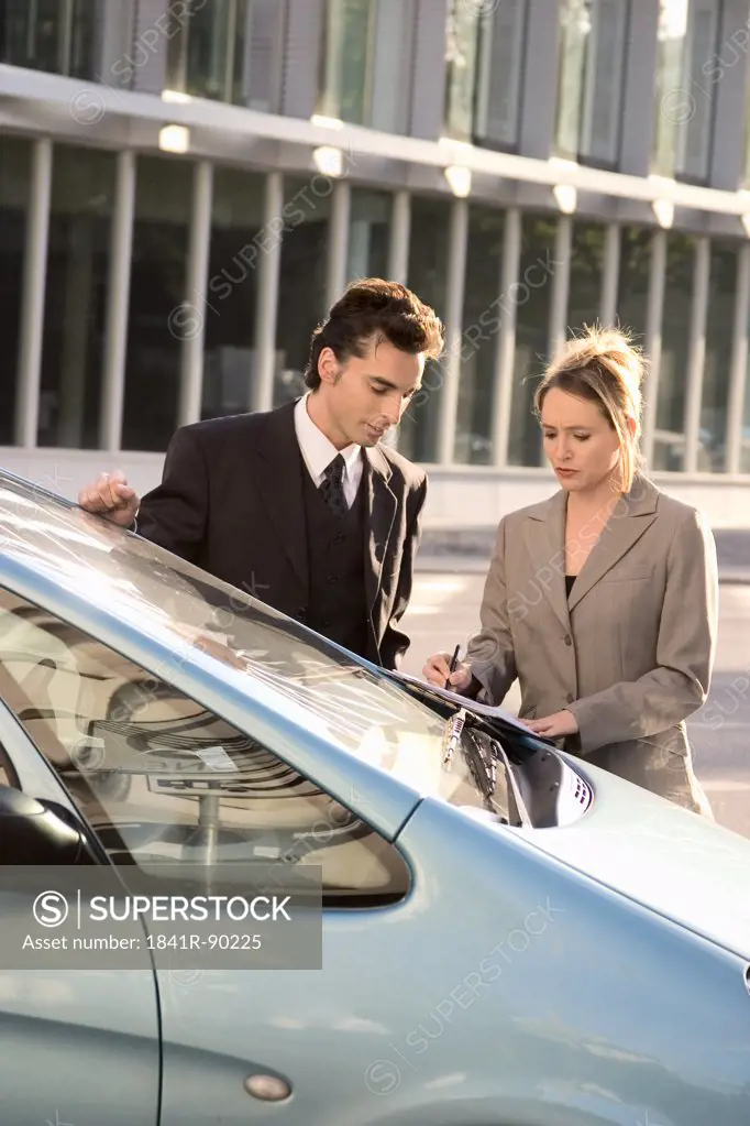 Businessman and businesswoman looking at document near car