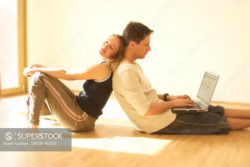 Side profile of young woman leaning against his husband working on laptop
