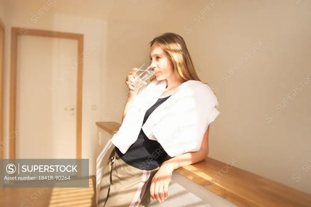 Young woman leaning against wall and drinking water