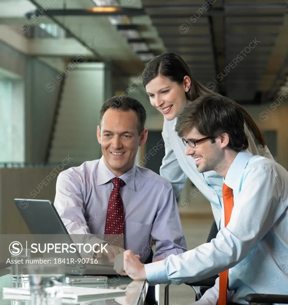 Three businesspeople looking at laptop in office