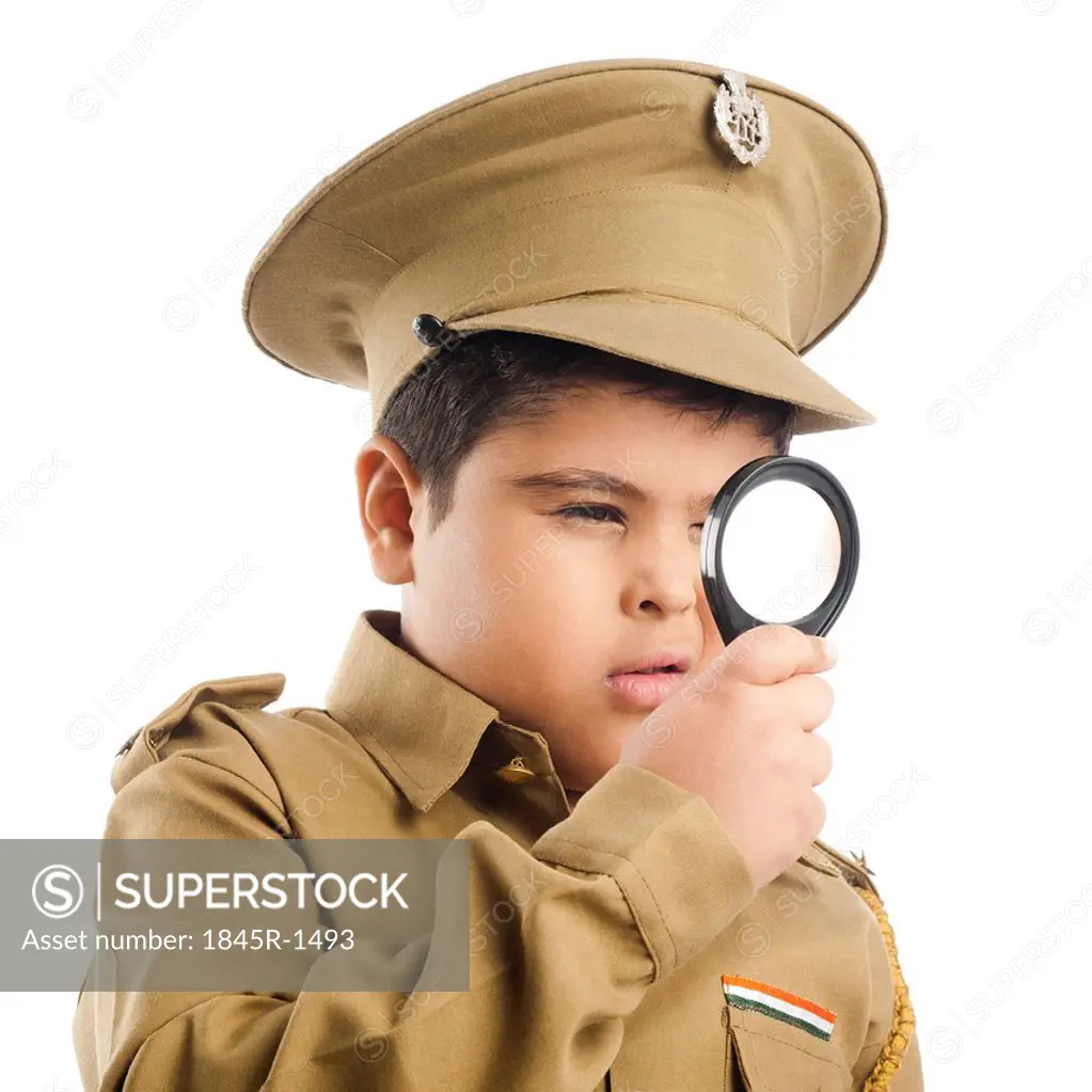 Close-up of a boy dressed as a police uniform looking through a magnifying glass