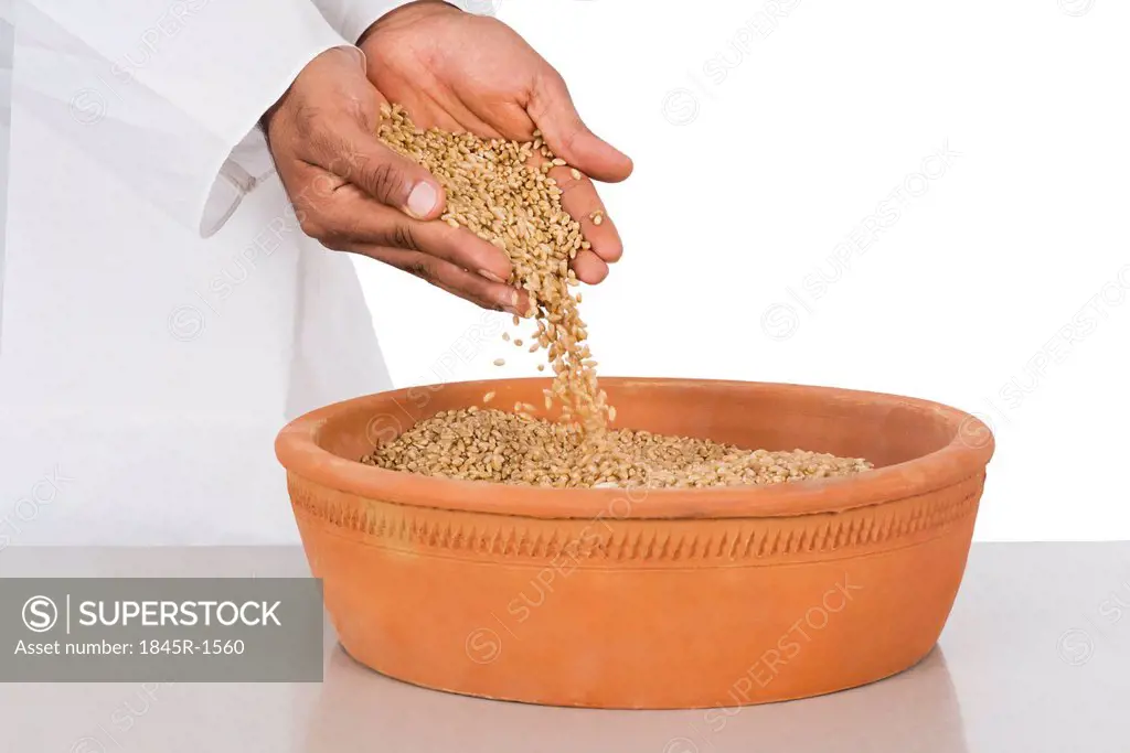 Human hand pouring wheat in a clay pot