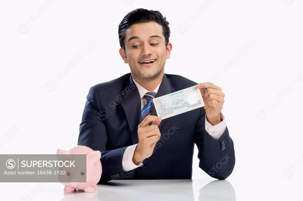 Businessman holding a currency note and looking at a piggy bank