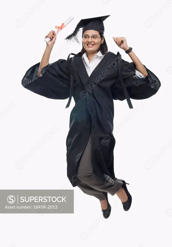 Woman jumping with her diploma in graduation gown