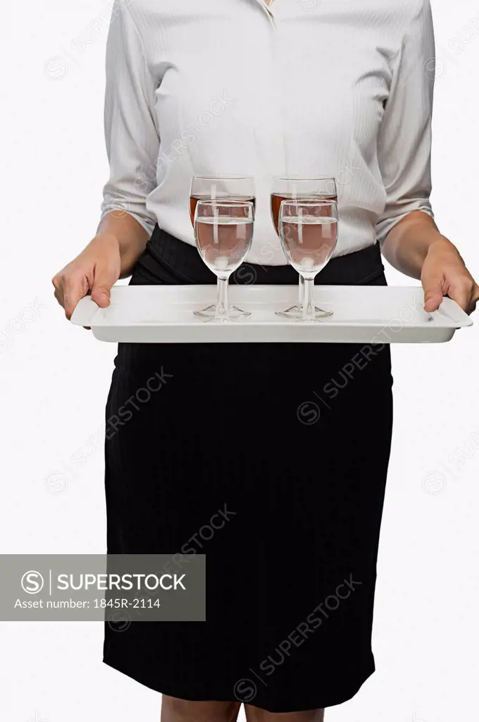 Mid section view of an air hostess carrying a tray of wine glasses