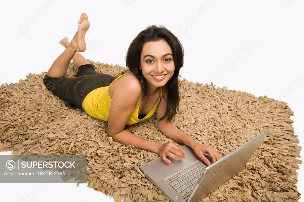 Woman lying on a rug and working on a laptop