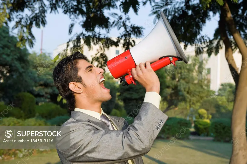 Businessman shouting into a megaphone in a park
