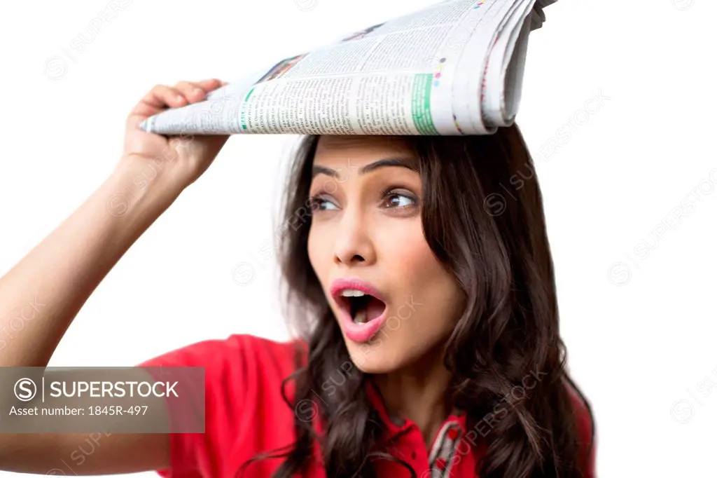 Close-up of a woman looking shocked with holding a newspaper
