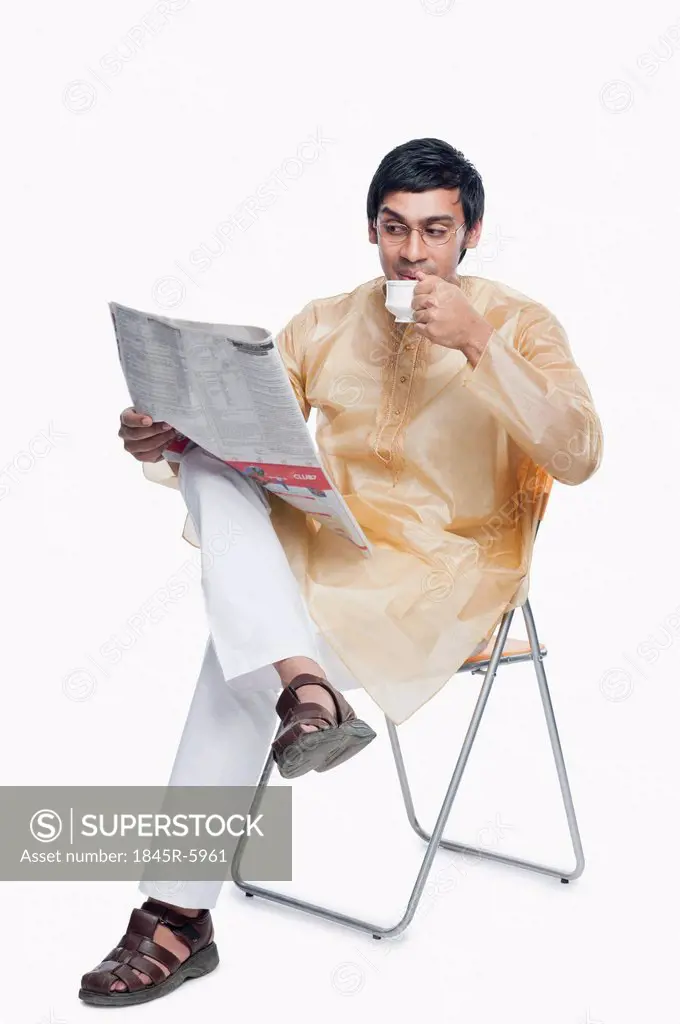 Bengali man reading a newspaper and having tea