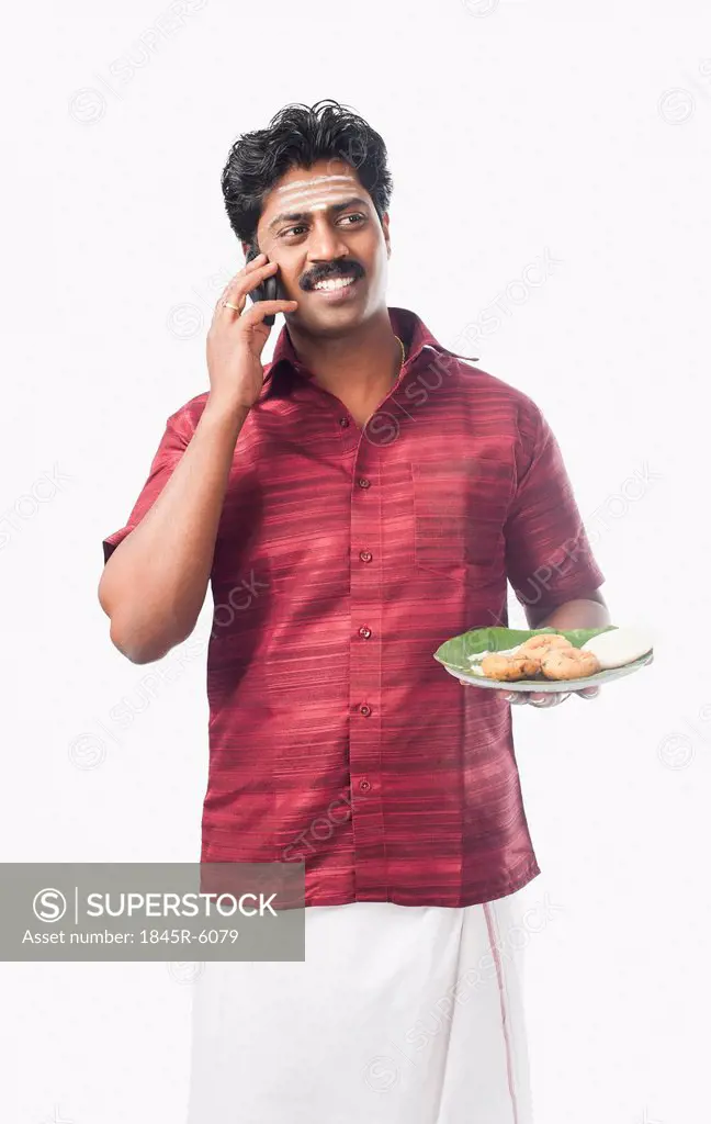 South Indian man holding a plate of food and talking on a mobile phone