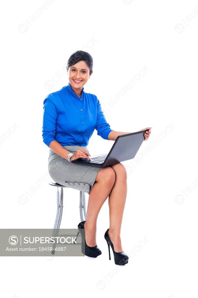 Businesswoman smiling while sitting on a stool and using a laptop