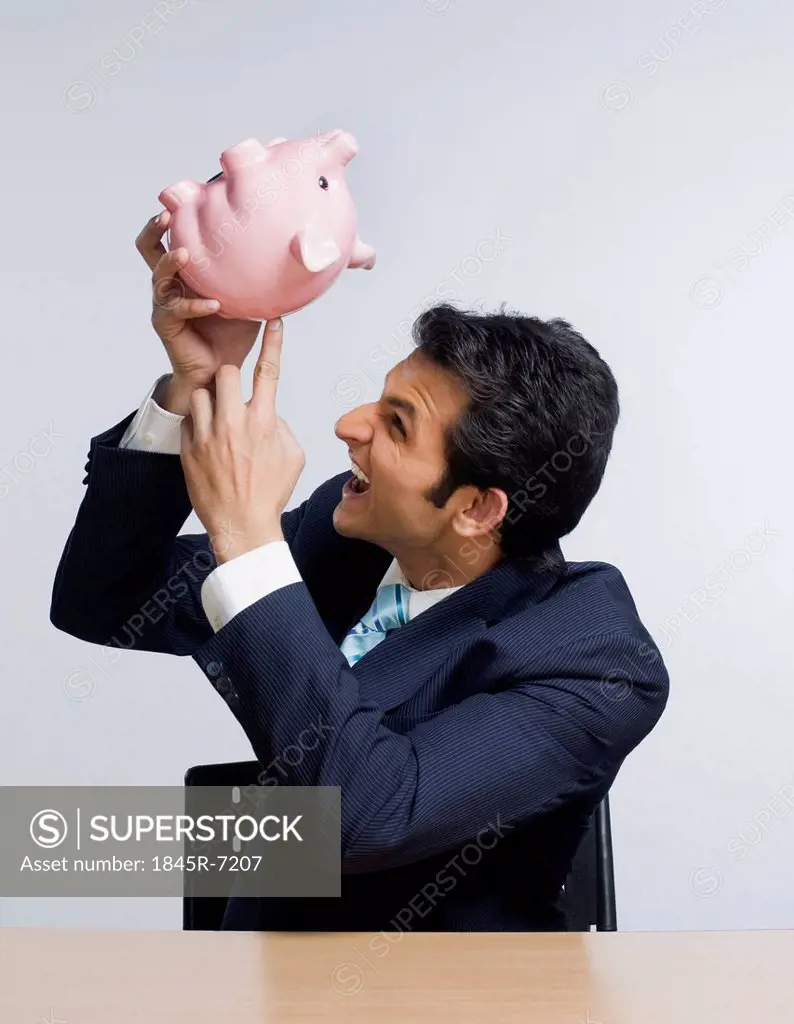 Businessman looking angry while emptying a piggy bank