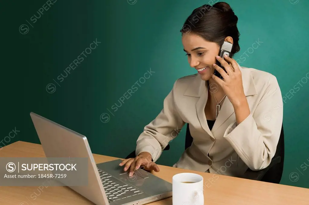 Businesswoman using a laptop and talking on a mobile phone
