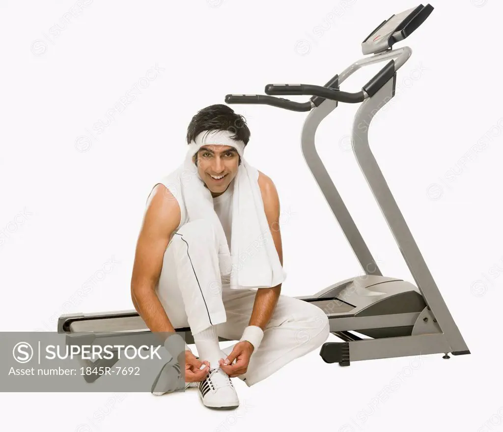 Man sitting on a treadmill and tying shoelaces