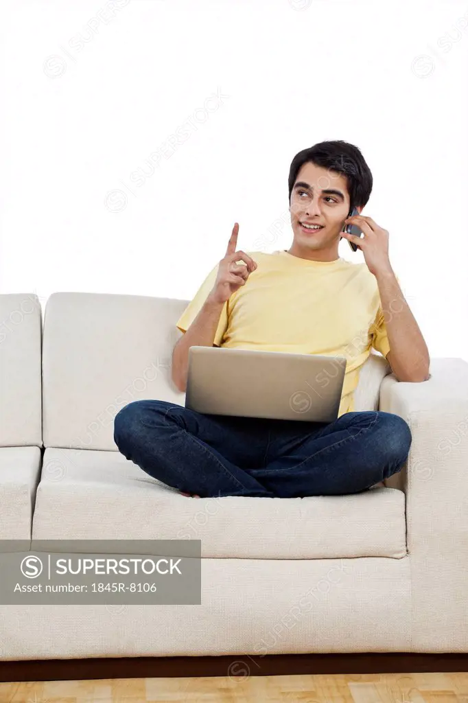 Man talking on a mobile phone and using a laptop at home