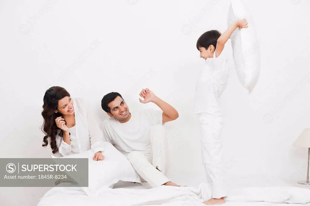 Happy boy pillow fight with his parents on the bed